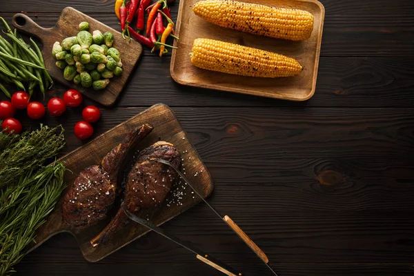 Vista superior da carne, milho, pimentas, tomates cereja, ervilhas verdes, vegetação, brotos de Bruxelas na tábua de corte, pinças — Fotografia de Stock
