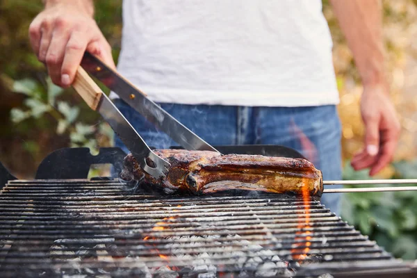 Cropped view of man with tweezers grilling meat on barbecue grid — Stock Photo