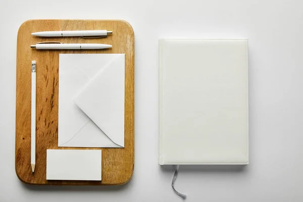 Top view of envelope, business card, pencil and pens on wooden board and notebook — Stock Photo