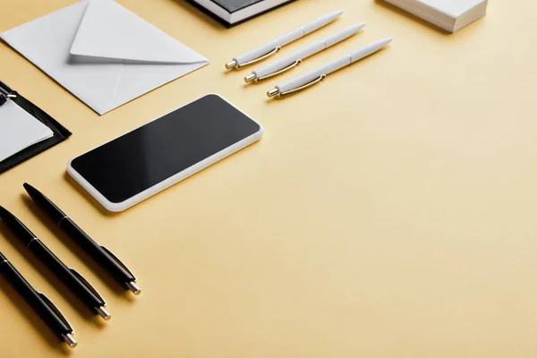 Конверт, ручки, визитки, смартфон с копировальным пространством на желтом фоне — стоковое фото