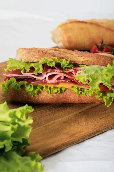 Selective focus of fresh sandwich with lettuce, ham, cheese, bacon and tomato on wooden cutting board — Stock Photo