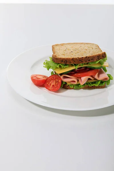 Свежий сэндвич с салатом, ветчиной, сыром, беконом и помидорами на белом фоне — стоковое фото