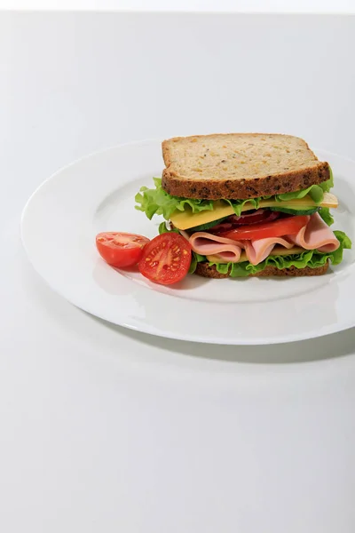 Sándwich fresco con lechuga, jamón, queso, tocino y tomate sobre fondo blanco - foto de stock