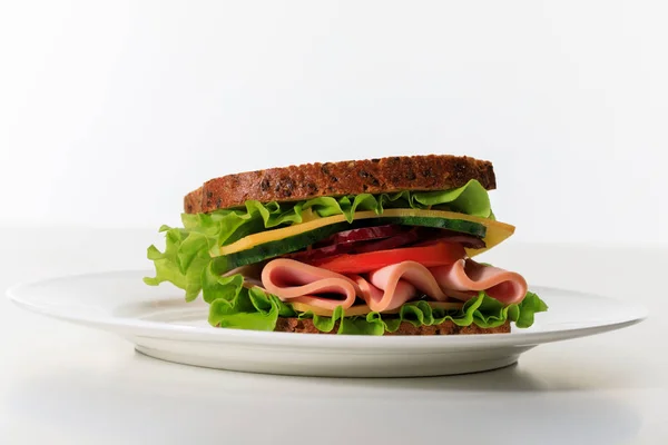 Fresh sandwich with lettuce, ham, cheese, bacon and tomato on plate isolated on white — Stock Photo