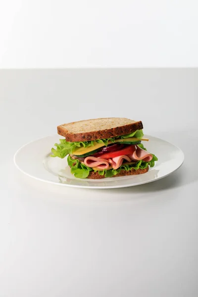Sanduíche fresco com alface, presunto, queijo, bacon e tomate em prato isolado em branco — Fotografia de Stock