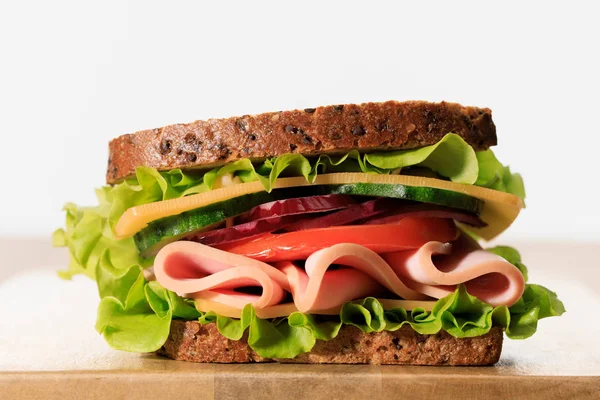 Fresh sandwich with lettuce, ham, cheese, bacon and tomato on wooden cutting board isolated on white — Stock Photo