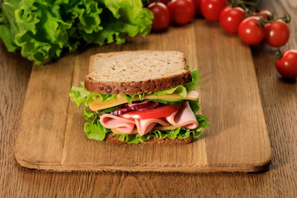 Selective focus of fresh sandwich on wooden cutting board near lettuce and cherry tomatoes — Stock Photo