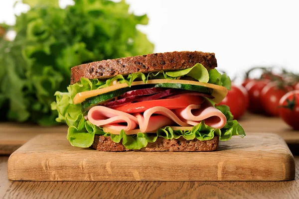 Sandwich frais avec laitue, jambon, fromage, bacon et tomate sur planche à découper en bois isolé sur blanc — Photo de stock