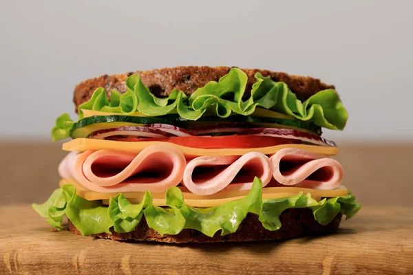 Panino fresco con lattuga, prosciutto, formaggio, pancetta e pomodoro su tagliere di legno isolato su grigio — Foto stock