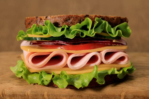 Fresh sandwich with lettuce, ham, cheese, bacon and tomato on wooden cutting board — Stock Photo