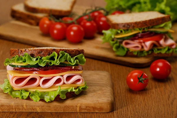 Focus selettivo di panino fresco con lattuga, prosciutto, formaggio, pancetta e pomodoro sul tagliere in legno — Foto stock