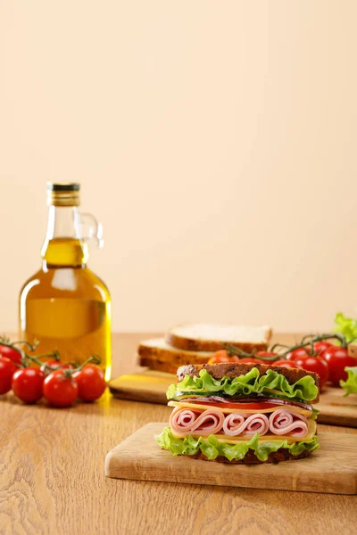 Foyer sélectif de sandwich frais près de laitue, pain, tomates cerises et huile sur table en bois isolé sur beige — Photo de stock
