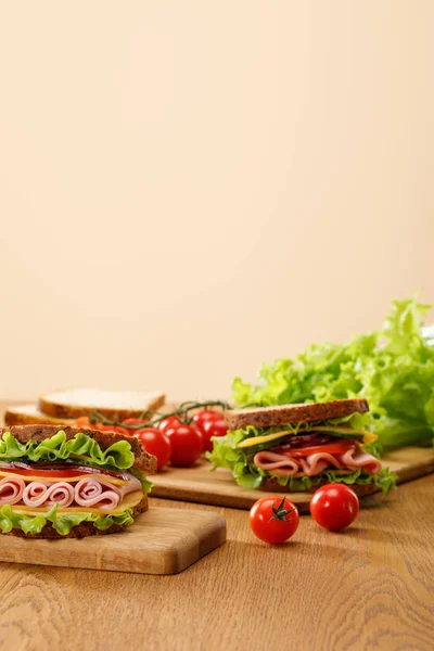 Selective focus of fresh sandwich near lettuce, bread, cherry tomatoes on wooden table isolated on beige — Stock Photo