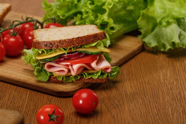 Selektiver Fokus des Sandwiches auf einem Holzschneidebrett in der Nähe von frischen Kirschtomaten und Salat — Stockfoto