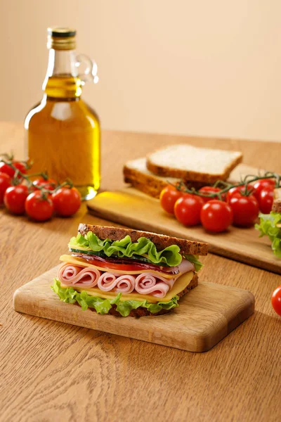 Selective focus of fresh sandwich near lettuce, bread, cherry tomatoes and oil on wooden table isolated on beige — Stock Photo