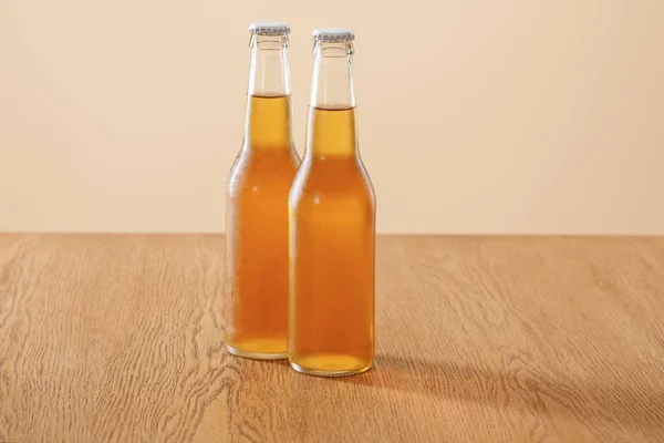 Bottles of beer at wooden table isolated on beige — Stock Photo