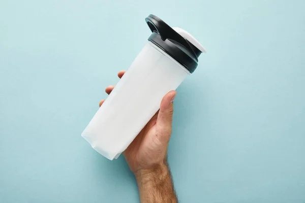 Vista cortada do homem segurando garrafa de esportes com batido de proteína no azul — Fotografia de Stock