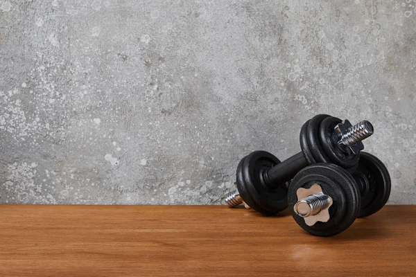 Pesadas y negras mancuernas sobre superficie de madera cerca de muro de hormigón - foto de stock