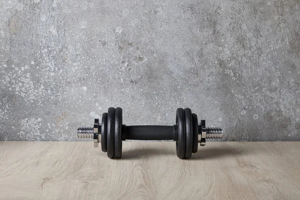 Heavy and black dumbbell on wooden surface near concrete wall — Stock Photo