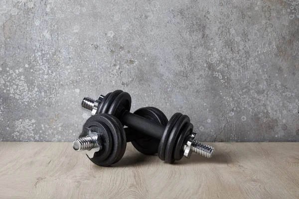 Heavy dumbbells on wooden surface near concrete wall — Stock Photo