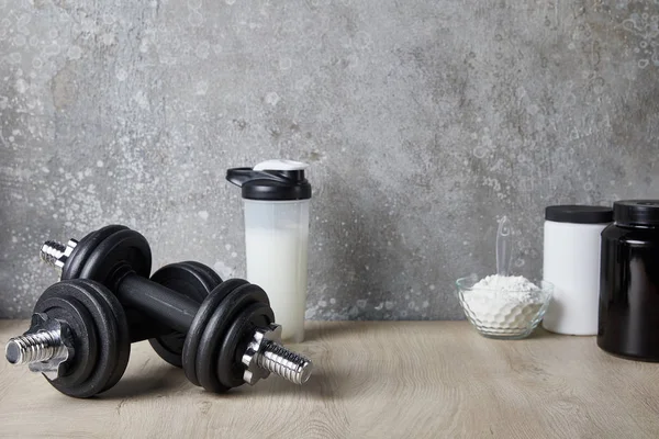 Proteinshake in Sportflasche in der Nähe von Kurzhanteln und Proteinpulver in der Nähe von Betonwänden — Stockfoto