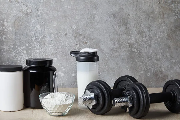 Dumbbells near protein shake in sports bottle and protein powder near concrete wall — Stock Photo