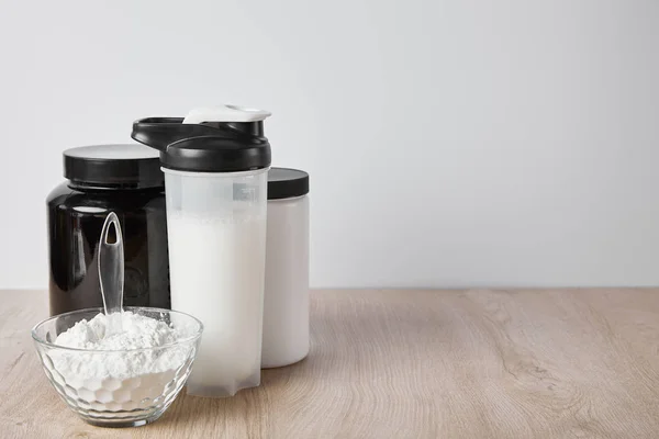 Garrafa de esportes com batido de proteína perto de frascos isolados em cinza — Fotografia de Stock