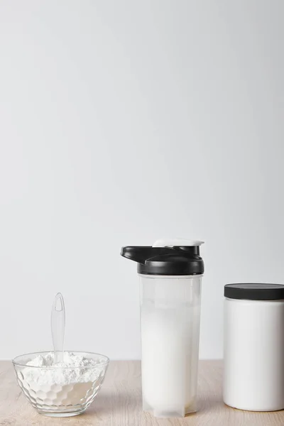 Protein shake in sports bottle near jar and glass bowl with protein shake isolated on grey — Stock Photo