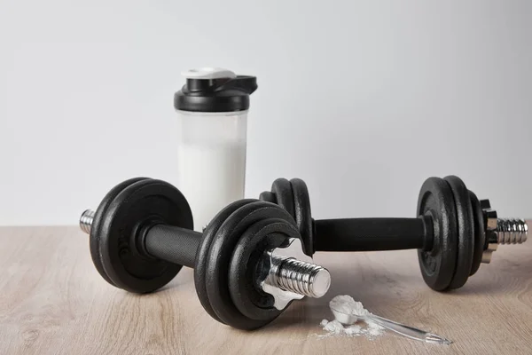 Cuchara con proteína en polvo cerca de pesas y botella deportiva aislada en gris - foto de stock