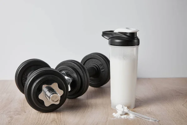 Cucchiaio con polvere proteica vicino ai manubri neri e bottiglia sportiva isolata su grigio — Foto stock