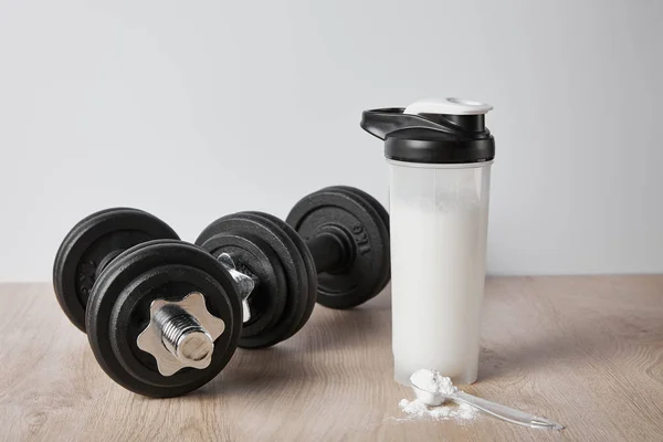 Colher com pó de proteína perto de halteres pretos e garrafa de esportes isolados em cinza — Fotografia de Stock