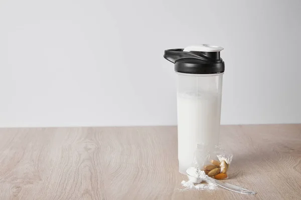 Sports bottle with protein shake near almonds isolated on grey — Stock Photo