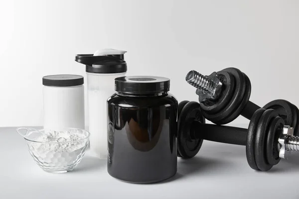 Manubri pesanti vicino a vasi e bottiglia sportiva con frullato proteico su bianco — Foto stock
