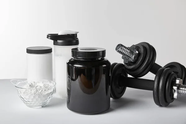 Halteres pesados perto de frascos e garrafa de esportes com batido de proteína no branco — Fotografia de Stock