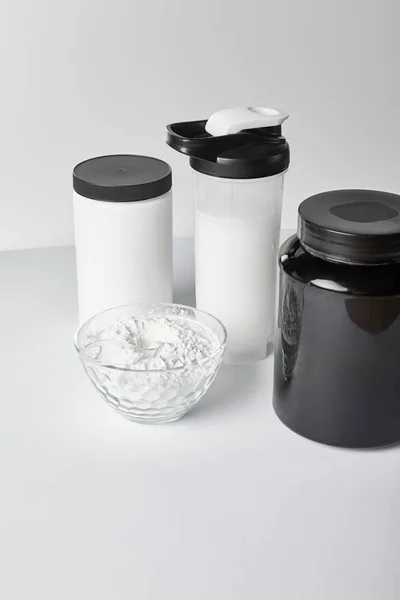 Barattoli e bottiglia sportiva con frullato proteico vicino ciotola con proteine in polvere su bianco — Foto stock