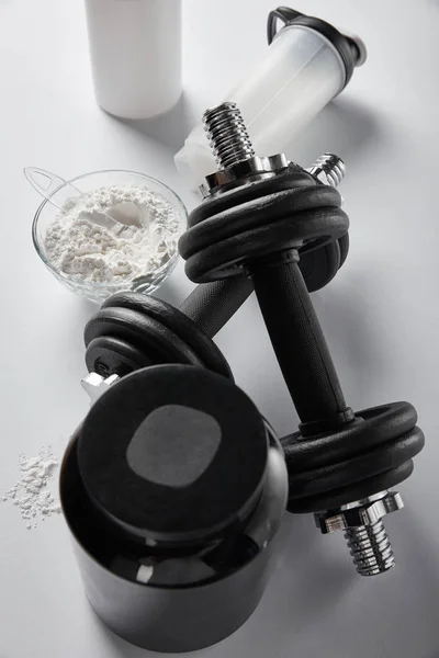 Top view of sports bottle near bowl with protein powder and dumbbells on white — Stock Photo