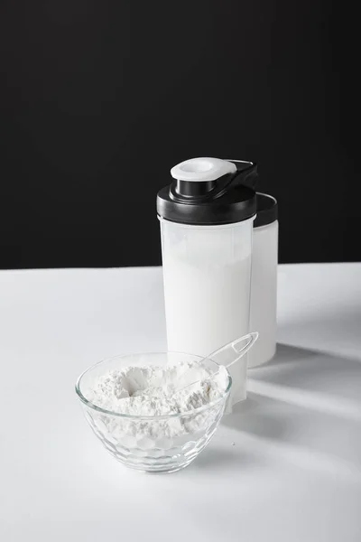 Ciotola di vetro con proteine in polvere vicino bottiglia sportiva e vaso su nero — Foto stock