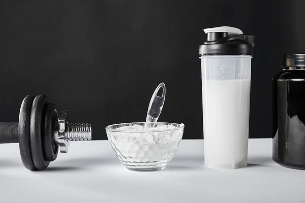 Schale in der Nähe von Hantel und Sportflasche mit Proteinshake auf schwarz — Stockfoto