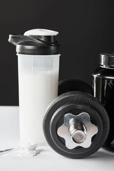 Spoon with protein near dumbbell and sports bottle with protein shake on black — Stock Photo
