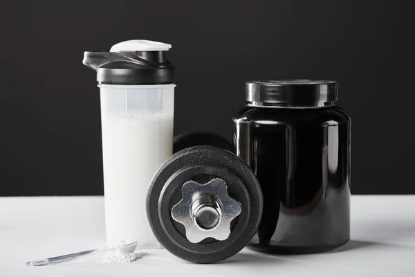 Cucchiaio vicino al manubrio e bottiglia sportiva con frullato proteico su nero — Foto stock