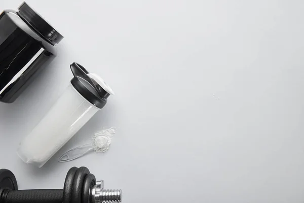 Top view of spoon with protein near dumbbell, jar and sports bottle on white — Stock Photo