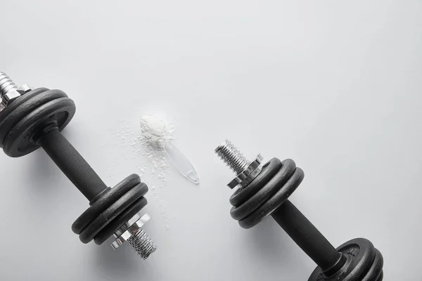 Vista superior da colher com pó de proteína perto de halteres pesados no branco — Fotografia de Stock