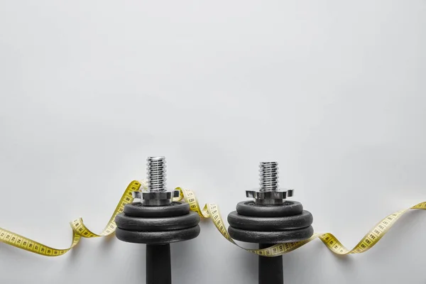 Top view of heavy black dumbbells near measuring tape on white — Stock Photo