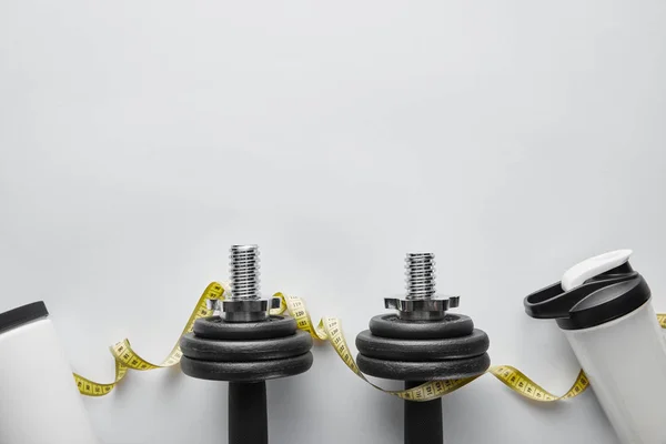 Top view of sports bottle and measuring tape near dumbbells on white — Stock Photo