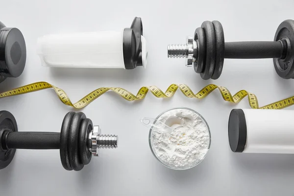 Vista superior de halteres pesados perto de garrafa de esportes e fita métrica em branco — Fotografia de Stock