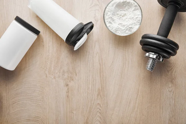 Vue de dessus de l'haltère près de la bouteille et du pot de sport sur la surface en bois — Photo de stock