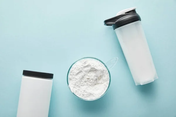 Top view of sports bottle near jar and glass bowl with protein powder on blue — Stock Photo