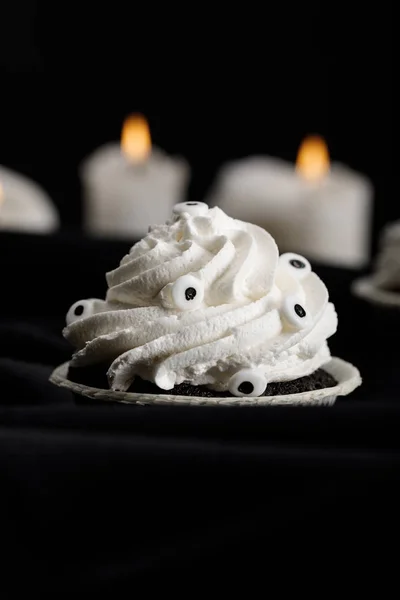 Selective focus of delicious Halloween cupcake with white cream near burning candles isolated on black — Stock Photo