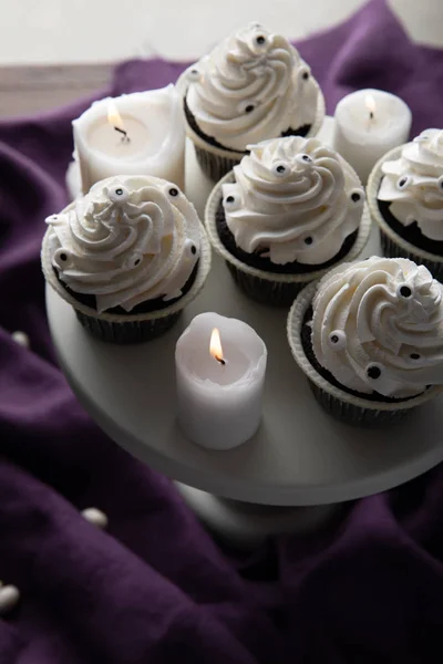 Delicious Halloween cupcakes on stand near burning candles on purple cloth — Stock Photo