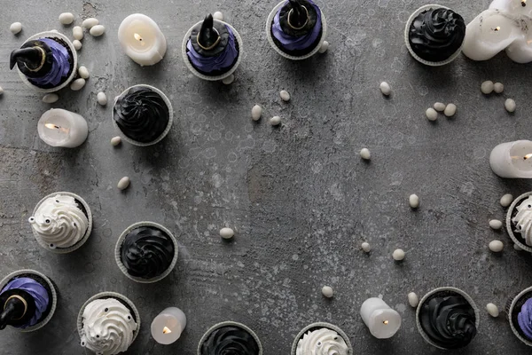 Vue du dessus de délicieux cupcakes d'Halloween avec des bougies allumées et des bonbons blancs sur une surface gris béton — Photo de stock